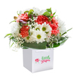 Infused with a sense of joy and renewal, this lush bouquet, nestled upright in an immaculate white gift bag, seems to gather the energy of spring mornings in Isleworth. Lively coral and striking red carnations, full and plush with ruffled petals, bring a touch of celebration to the display, as if echoing the blooming flowerbeds of Syon Lane. Bright white daisies, their golden-green centres gleaming, provide a crisp, cheerful contrast, suggesting optimism and the playful laughter of community gatherings along St John's Road. Wispy baby's breath, scattered delicately throughout, lends a gentle softness, lightening the whole ensemble-much like the calming presence of Isleworth's riverside paths. The addition of unopened buds tinged with purple on one side introduces an undertone of mystery and possibility, drawing the eye and inviting curiosity. Beneath it all, abundant deep green foliage with broad, shiny leaves supports and frames the arrangement, grounding it in lushness and vitality. Crafted into a perfectly rounded silhouette, the bouquet expresses not only freshness but genuine care and skill, as you'd expect from Isleworth's favourite flower specialists. The white gift bag, finished with wide satin ribbon handles and a discreet, stylish logo, promises both convenience and elegance for delivery or gifting. Photographed against a flawless white backdrop, the ensemble glows with a sense of clarity and hope-just the bouquet to say 'Congratulations,' mark a birthday, or send heartfelt wishes to someone special in Isleworth.